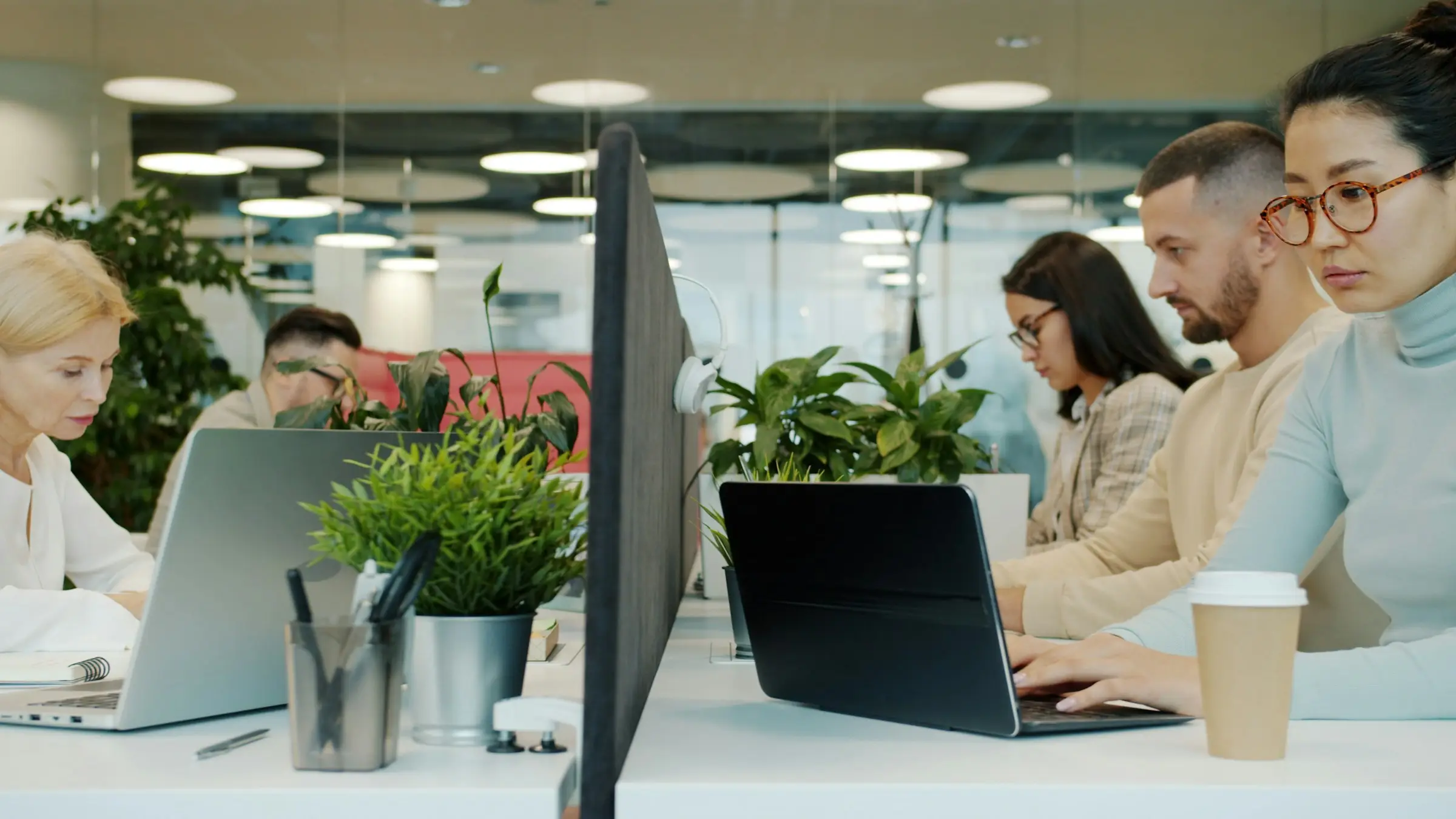 Offener Arbeitsraum mit mehreren Arbeitsplätzen, Menschen arbeiten an Laptops.
